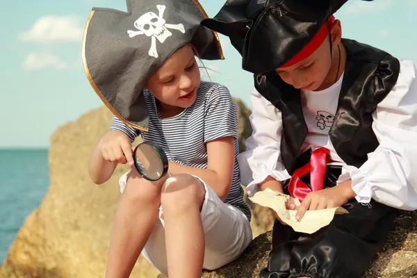 Радостная маленькая девочка и мальчик в маскарадных костюмах пират сидит на берегу моря — стоковое фото
