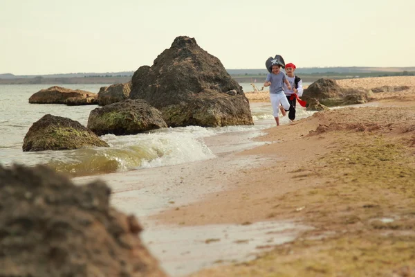 Vidám, boldog aranyos fiú és lány, kalóz jelmezek mezítláb fut, a tenger partján — Stock Fotó