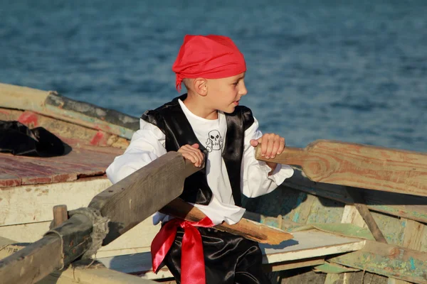 Мальчик, одетый как пират, плывет на старой лодке в море. — стоковое фото