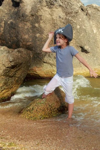 Charming young girl in a pirate hat standing in water at the beach in summer — Stock Photo, Image