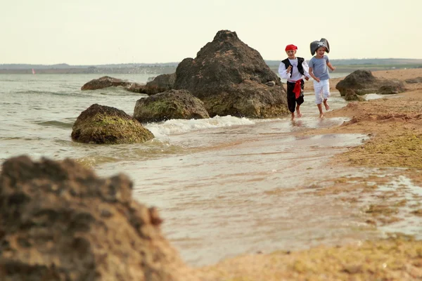 Cheerful happy cute boy and girl in pirate costumes barefoot run along the sea coast — Stock Photo, Image