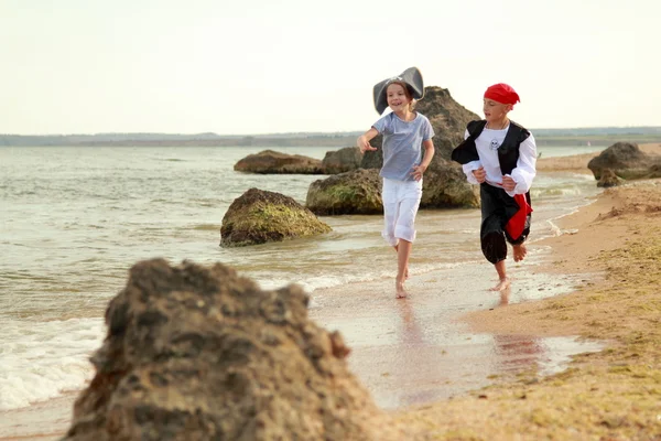 Vrolijke gelukkig schattige jongen en meisje in piraat kostuums blootsvoets lopen langs de zeekust — Stockfoto