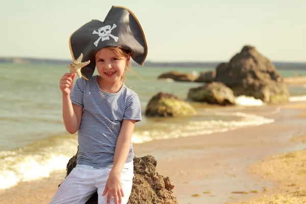 Menina bonita em chapéu de pirata com um crânio segurando uma estrela do mar na praia — Fotografia de Stock