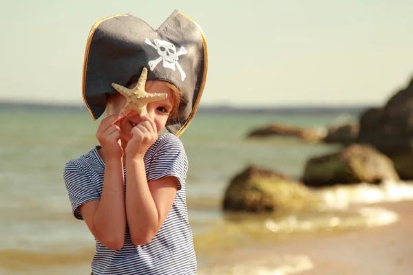 Chica joven dulce caucásica en un sombrero pirata con una estrella de mar sobre un fondo de un paisaje marino —  Fotos de Stock