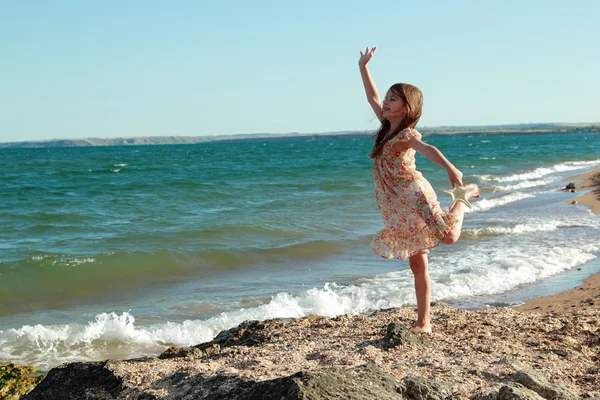Szép vidám mosolygós kislány táncol a parton a nyári napsütésben — Stock Fotó