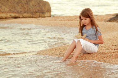 güzel bir kız ile uzun saç ve sağlıklı su deniz kıyısında ve wets ayaklarda ciltte.