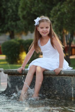Havuzun oturan ve yaz Tema gülümseyerek beyaz elbiseli neşeli sevimli küçük kız