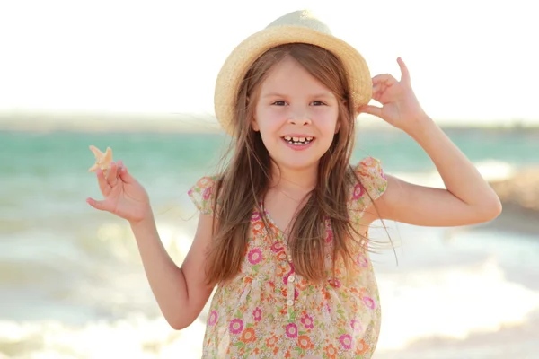 Smiling young girl holding a starfish sitting on the bank of the summer sea. — Stok fotoğraf