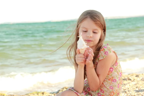 Portret van een schattig klein meisje met dromen van een glimlach en houden een zeeschelp — Stockfoto