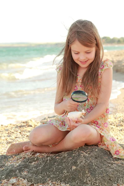 Neşeli genç kız bir büyüteç seashell beach yaz deniz üzerinde ele alıyor. — Stok fotoğraf