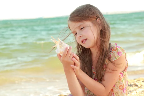 Retrato de uma menina bonita com sonhos de um sorriso e segurando uma concha — Fotografia de Stock