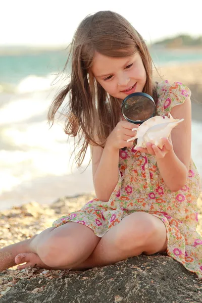 Jovencita alegre examina una lupa de concha marina en la playa de verano mar — Foto de Stock