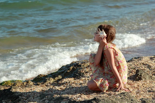 Portrait of a cute little girl with dreams of a smile and holding a seashell. — Stock Photo, Image