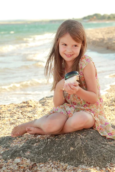 Glada unga flickan undersöker en förstoringsglas snäcka på stranden sommaren havet. — Stockfoto