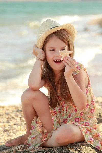 Menina bonita segurando uma estrela do mar sentado na margem do mar de verão . — Fotografia de Stock