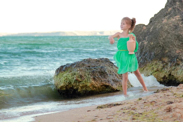 Adorable little girl in a green tunic holds ancient amphora.