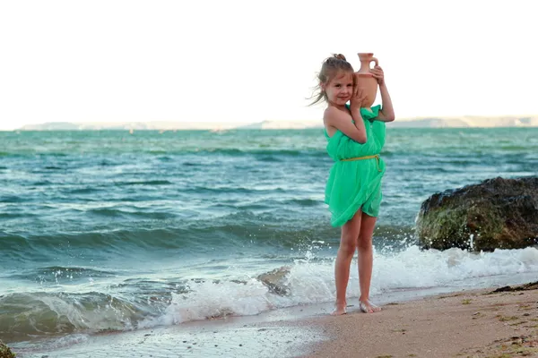Grekiska leende liten flicka i tunika innehar antika Amfora. — Stockfoto