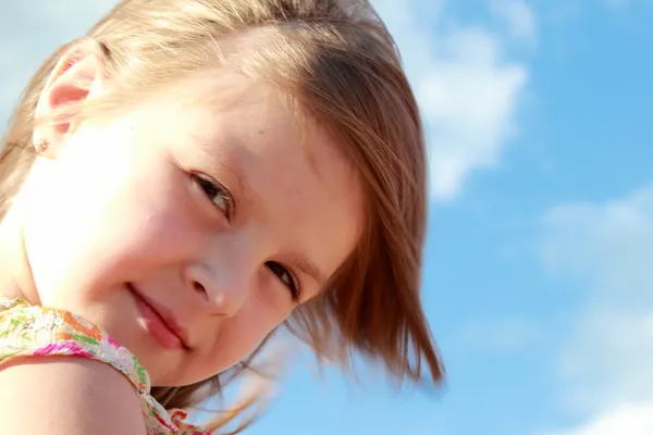 Porträtt av söta leende liten flicka på en bakgrund av blå himmel med moln utomhus. — Stockfoto