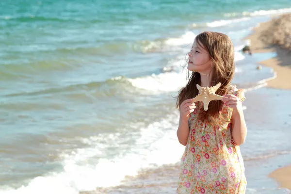 Adorable niña feliz sosteniendo una estrella de mar en la playa en el día soleado . — Foto de Stock
