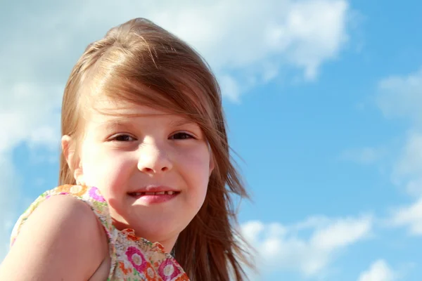 Portrét roztomilý usměvavá holčička na pozadí modré oblohy mraky venku. — Stock fotografie