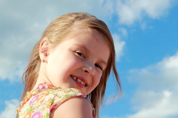 Retrato de linda niña sonriente sobre un fondo de cielo azul con nubes al aire libre . — Foto de Stock