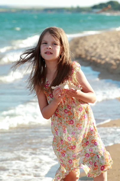 Adorable petite fille heureuse tenant une étoile de mer sur la plage dans la journée ensoleillée . — Photo