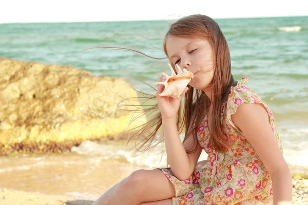 Adorável menina feliz segurando uma concha na praia do mar em um dia ensolarado . — Fotografia de Stock