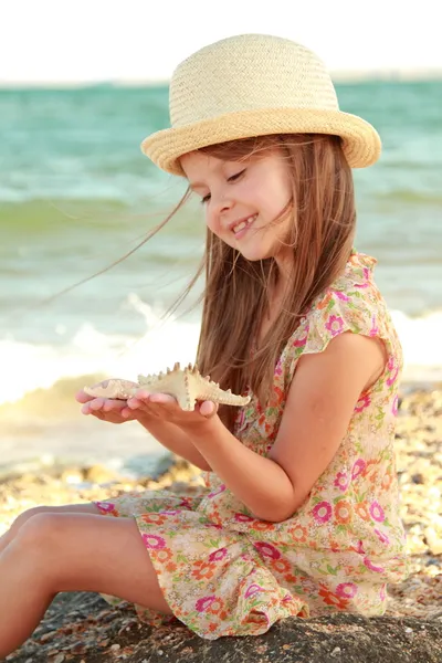 Caucasiano bonito menina em um vestido de verão e chapéu segurando uma estrela do mar . — Fotografia de Stock