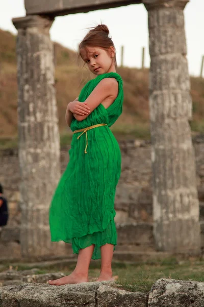 Adorable little girl in the emerald dress on a background of ancient sites of the ancient Greek city of Patikapey. — Stock Photo, Image