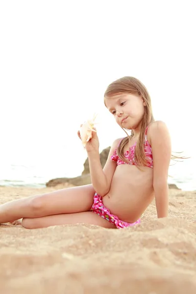Portret van een glimlachende vrij klein meisje in een zwembroek houden een mooie zeeschelp. — Stockfoto