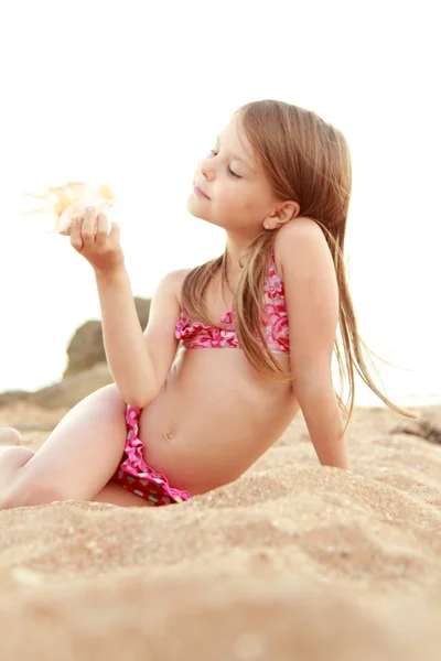 Linda chica feliz con una sonrisa encantadora jugando en la arena con una concha de mar . — Foto de Stock