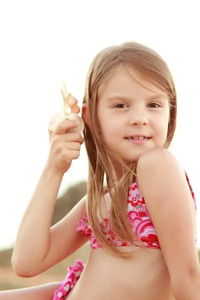 Bir deniz kabuğu kumla oynayan bir mayo güzel küçük kız. — Stok fotoğraf