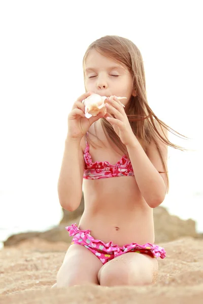 Caucasian happy young girl in a pink swimsuit sitting on the beach. — Stock Photo, Image