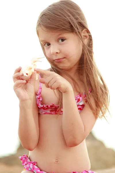 Beautiful cheerful young girl sitting on the sand and holds a large seashell. — Stock Photo, Image