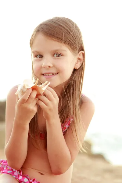 Cute smiling little girl in a bathing suit sits on a background of sea sand. — Stock Photo, Image