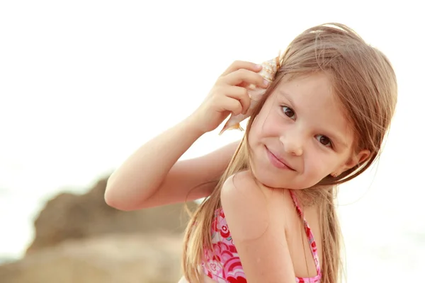 Linda chica feliz con una sonrisa encantadora jugando en la arena con una concha de mar — Foto de Stock