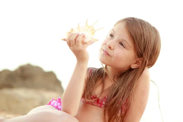Mooie vrolijke jonge meisje, zittend op het zand en bezit een grote zeeschelp. — Stockfoto