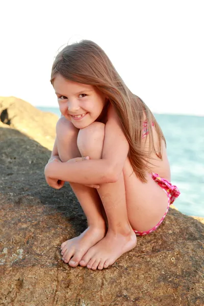 Nettes kleines Mädchen im Badeanzug sitzt auf einem großen Felsen am Meer. — Stockfoto