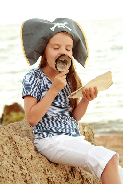 Bela menina alegre em um traje de pirata está estudando um mapa do tesouro . — Fotografia de Stock