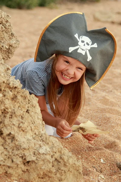 Hermosa niña con un disfraz de pirata con una sonrisa malvada está sosteniendo un mapa . — Foto de Stock