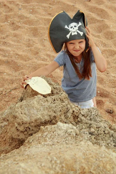 Menina bonito em um chapéu de pirata com um mapa pirata na mão em um fundo de mar . — Fotografia de Stock