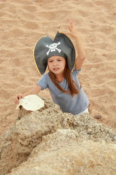 Gyönyörű kis lány, egy gonosz vigyorral kalóz jelmez megjelenítése gazdaság, és keresi a kincset a strandon. — Stock Fotó