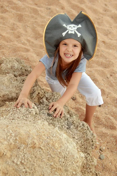 Aranyos kislány keresi meg a kincset a strandon egy napsütéses napon kalóz kalap. — Stock Fotó