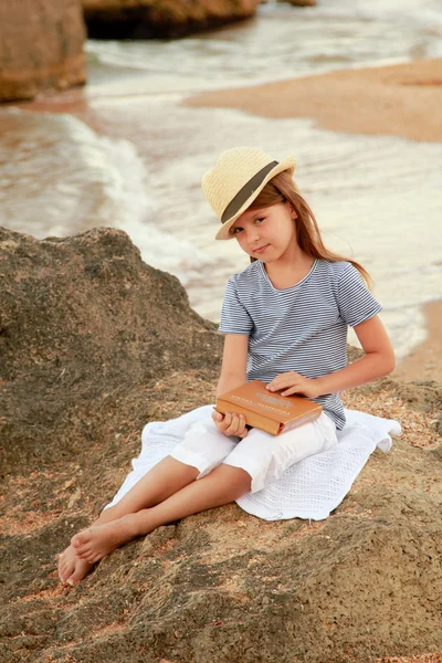 Caucasian smiling young girl in casual clothes reading a book on the beach on a summer day. — Stock Photo, Image