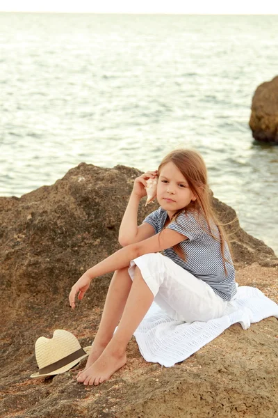 素敵な笑顔で幸せなかわいい女の子は、夕方にビーチに座っています。. — ストック写真