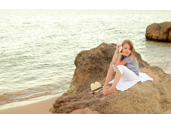 Happy cute little girl with a beautiful smile is sitting on the beach in the evening. — Stock Photo, Image