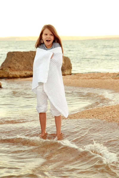 Positiva sonrisa niña en la playa moja los pies en el agua al atardecer en el aire libre . — Foto de Stock