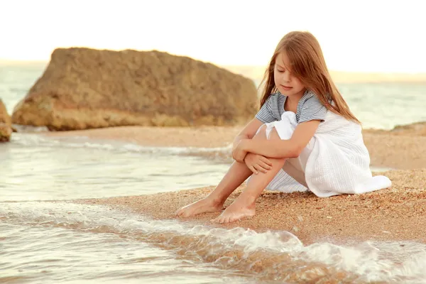 Positive smiling little girl on the beach wets feet in water at sunset on the outdoor. — Stock Photo, Image