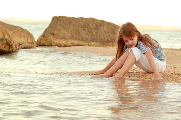 Красивая девушка с длинными волосами и здоровой кожей на берегу моря и мочит ноги в воде . — стоковое фото