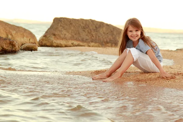 Hermosa chica con el pelo largo y la piel sana en la orilla del mar y moja los pies en agua . —  Fotos de Stock